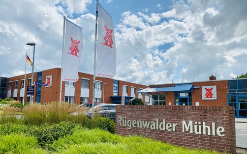 Das Werk der Rügenwalder Mühle in Bad Zwischenahn in Niedersachsen. Auf Fahnen und am Hauptgebäude ist die Rote Mühle zu sehen, das Markenzeichen der Rügenwalder Mühle